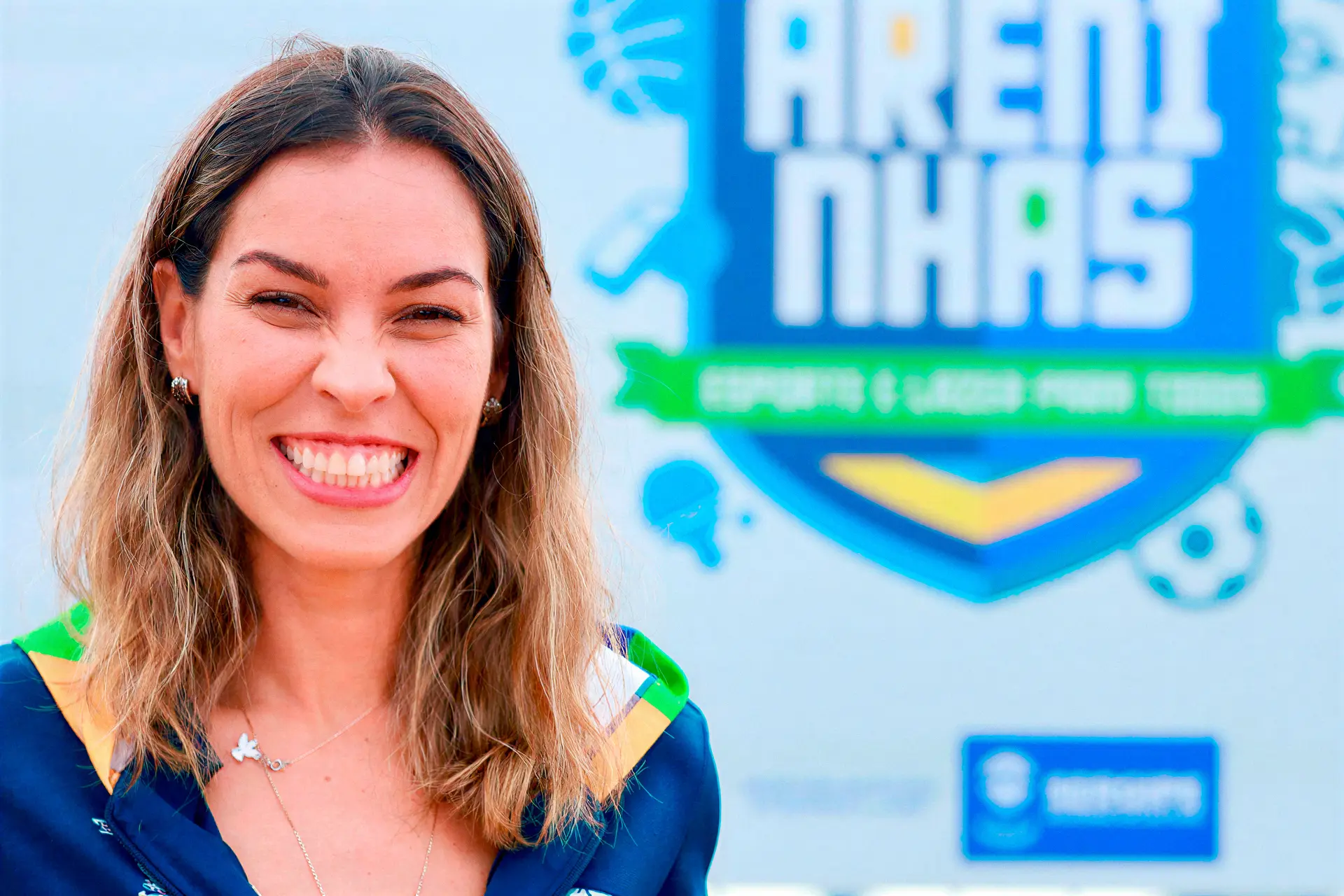 Mariana Dantas sorrindo em frente ao painel das Areninhas de Esporte e Lazer