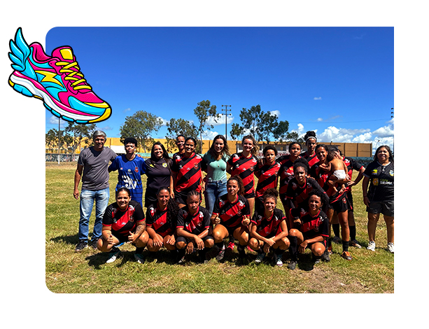 Equipe de futebol feminino reunida para foto em campo com Mariana Dantas